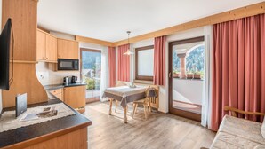 A modern kitchen with wooden cabinets, a microwave, and a dining area with a table and chairs. - Apartment 'Prapoz Typ A' with Mountain View, Balcony & Wi-Fi (Ortisei)