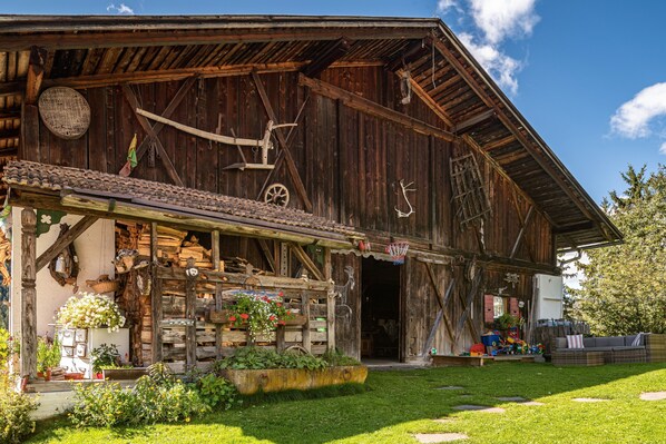 A rustic wooden barn with a covered porch, a basketball hoop, and a garden area with flowers and plants.