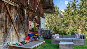 A rustic wooden building with a play area, a wicker sofa, and a small table. - Apartment 'Prapoz Typ B1' with Mountain View, Shared Garden & Wi-Fi (Ortisei)