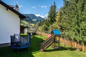Un jardin avec un trampoline, une cabane et une vue sur une montagne.