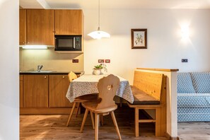 Une cuisine compacte avec des meubles en bois, un four à micro-ondes, une table à manger avec des chaises, un banc et un luminaire fixé au mur.