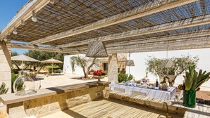 Ett utomhusområde med plats för måltider, utrustat med bord i sten, parasoller och en pergola.