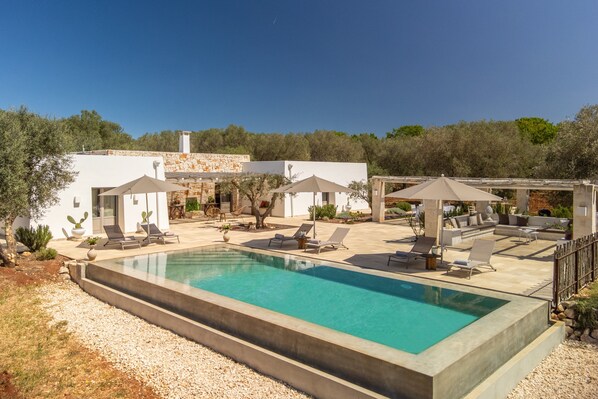 A modern pool area with lounge chairs, umbrellas, and a clear blue pool.