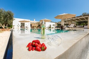 A poolside area with a bottle, glasses, and strawberries.