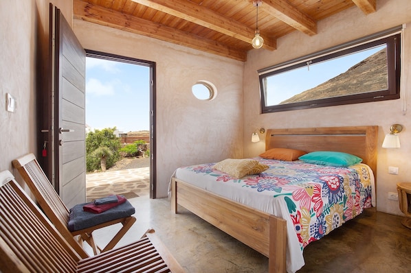 A bedroom with a wooden bed, a bench, a window, and a view of the outdoors.