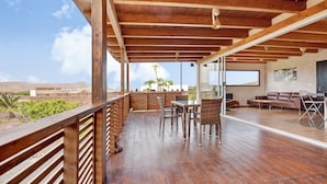 A spacious outdoor deck with wooden flooring, a dining area with chairs and a table, and a seating area with sofas and a TV. - Tayu Eco Villa – Mountain Views, Garden & Pool in Villaverde (Villaverde)