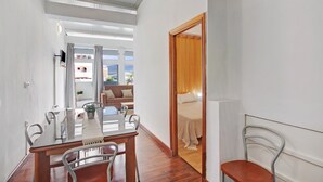 Ett modernt hotellrum med ett matbord och stolar i trä, en säng med ett huvudgavel i trä, en tv som är monterad på väggen och utsikt över staden genom stora fönster.