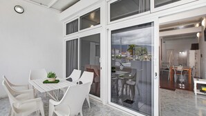 En modern inredning med ett matområde, en skjutdörr i glas som leder ut till en balkong och ett köksområde som syns genom dörren.