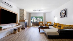 Uma sala de estar com televisão de tela plana, lareira, sofá e mesa de jantar.
