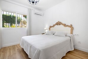 Ein Schlafzimmer mit einem Bett, einem Fenster mit Gitterstäben, einer Klimaanlage, einer Lampe und einer Steckdose.