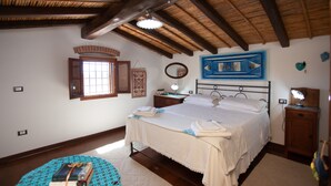 A bedroom with a bed, wooden beams, a window, a bedside table, and a wall-mounted mirror. - Holiday Home "Sa Domedda" with Mountain View, Garden & A/C (Orosei)