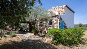 A stone building with a blue door, surrounded by greenery and a paved area with outdoor furniture. - Holiday Home "Sa Domedda" with Mountain View, Garden & A/C (Orosei)