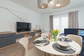A modern living room with a dining area, a flat-screen TV, and a sofa.