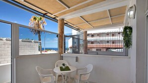 Un balcón con una mesa y sillas, vista al mar y una palmera.