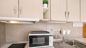 Una cocina con microondas integrado, lavamanos de acero inoxidable y armarios de tonos claros.