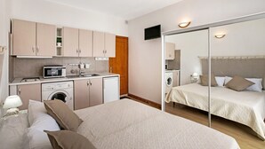Habitación de hotel compacta con kitchenette, una cama, lavadora y espejo.