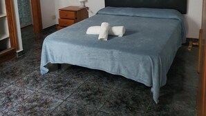 Een slaapkamer met een bed, nachtkastje, lamp en een handdoek op het bed.