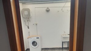 Een wasruimte met een wasmachine, een wasbak en betegelde vloer.