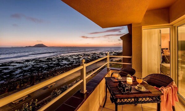Un balcon donnant sur l’océan, avec une vue imprenable au coucher du soleil, une table avec une bougie et une chaise.