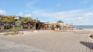 A wooden deck with outdoor seating, a restaurant with a view, and a building with a sign. - Vacation Apartment '7even' with Sea View, Balcony and Wi-Fi (Corralejo)
