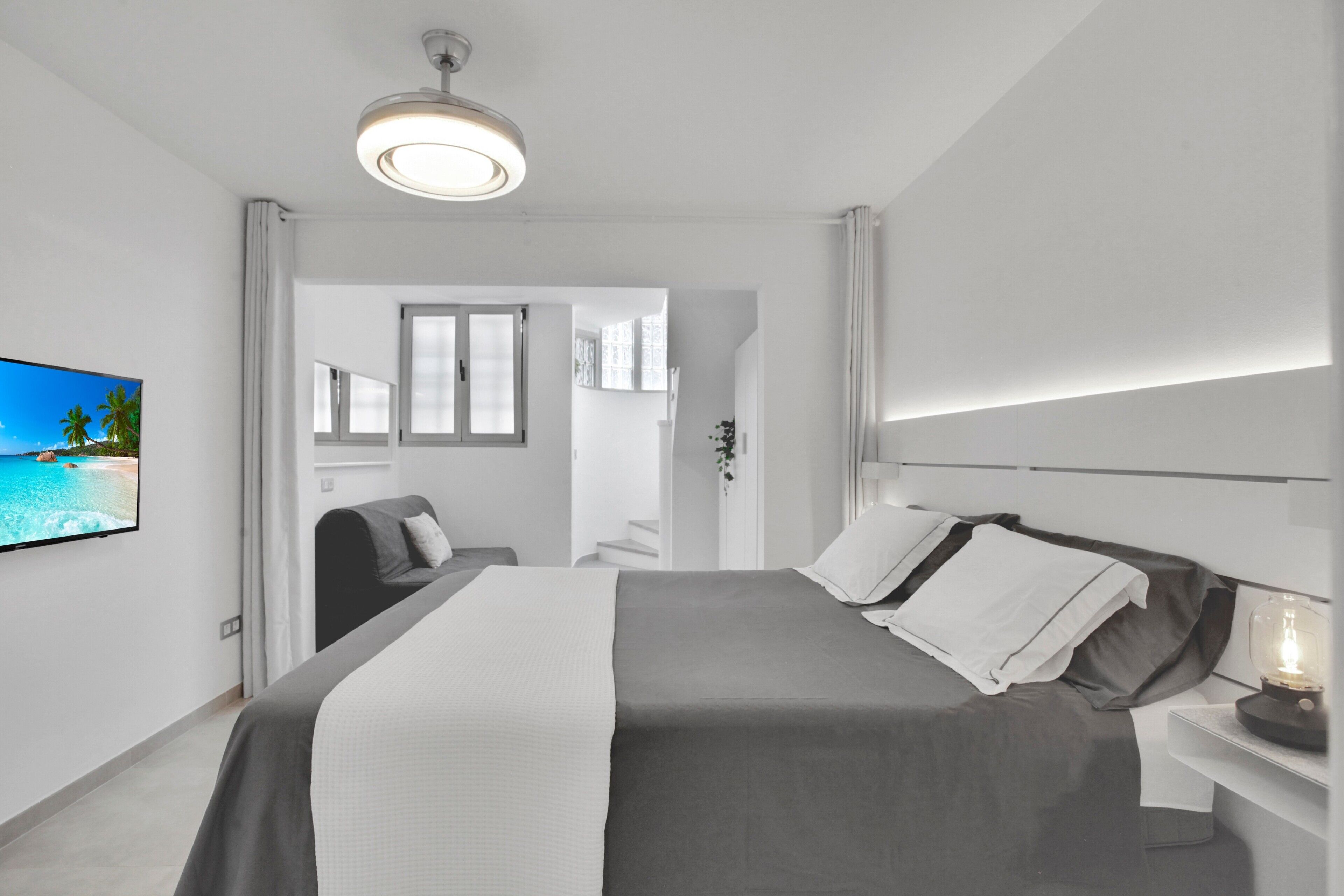 A modern hotel room with a large bed, a flat-screen TV, a bedside table with a lamp, and a view of the sea through the window.