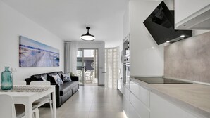A modern kitchen with white cabinetry, a dining area with a white table and chairs, and a living area with a black sofa. - Vacation Apartment '7even' with Sea View, Balcony and Wi-Fi (Corralejo)