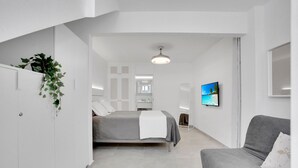 A modern bedroom with a bed, a grey sofa, a TV, and a plant. - Vacation Apartment '7even' with Sea View, Balcony and Wi-Fi (Corralejo)