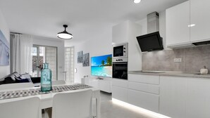 A modern kitchen with white cabinetry, a built-in oven, a microwave, and a flat-screen TV. - Vacation Apartment '7even' with Sea View, Balcony and Wi-Fi (Corralejo)