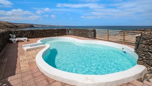 En swimmingpool med en stenvæg og udsigt til havet.