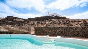 Una piscina con un muro de piedra y un edificio blanco al fondo.