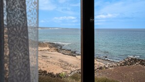 Vista costera a través de una ventana con cortina estampada, costa rocosa y mar tranquilo.