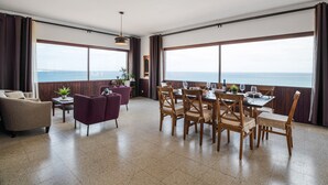 Un área de comedor con vista al mar, sillas de madera, una mesa dispuesta para comer y un sofá.