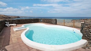 Una piscina con pared de piedra y vista al océano.
