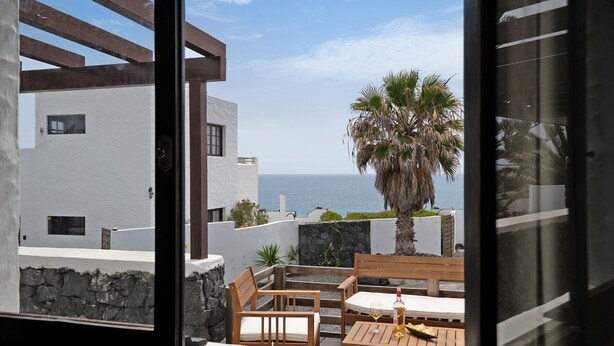 Un balcón con mobiliario de madera, una mesa con una botella y vista al mar.