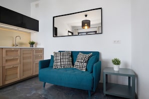A modern kitchen with wooden cabinets, a teal sofa with patterned cushions, and a small side table with a plant.