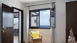 Una habitación con una silla de mimbre, un ventanal con vistas y una puerta que da a un espacio exterior.