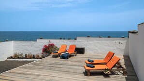 A rooftop terrace with wooden flooring, orange lounge chairs, and a view of the ocean.