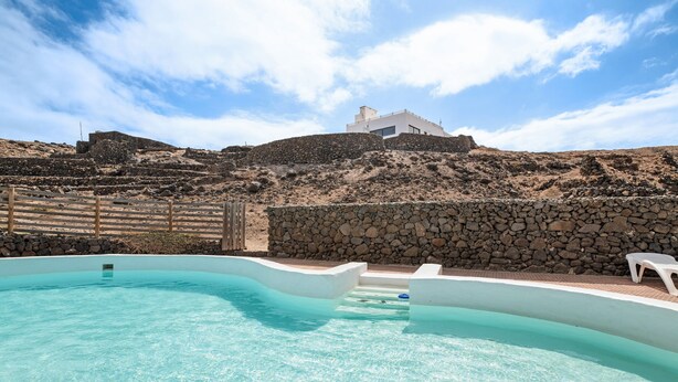 A swimming pool with a stone wall and a white building in the background.