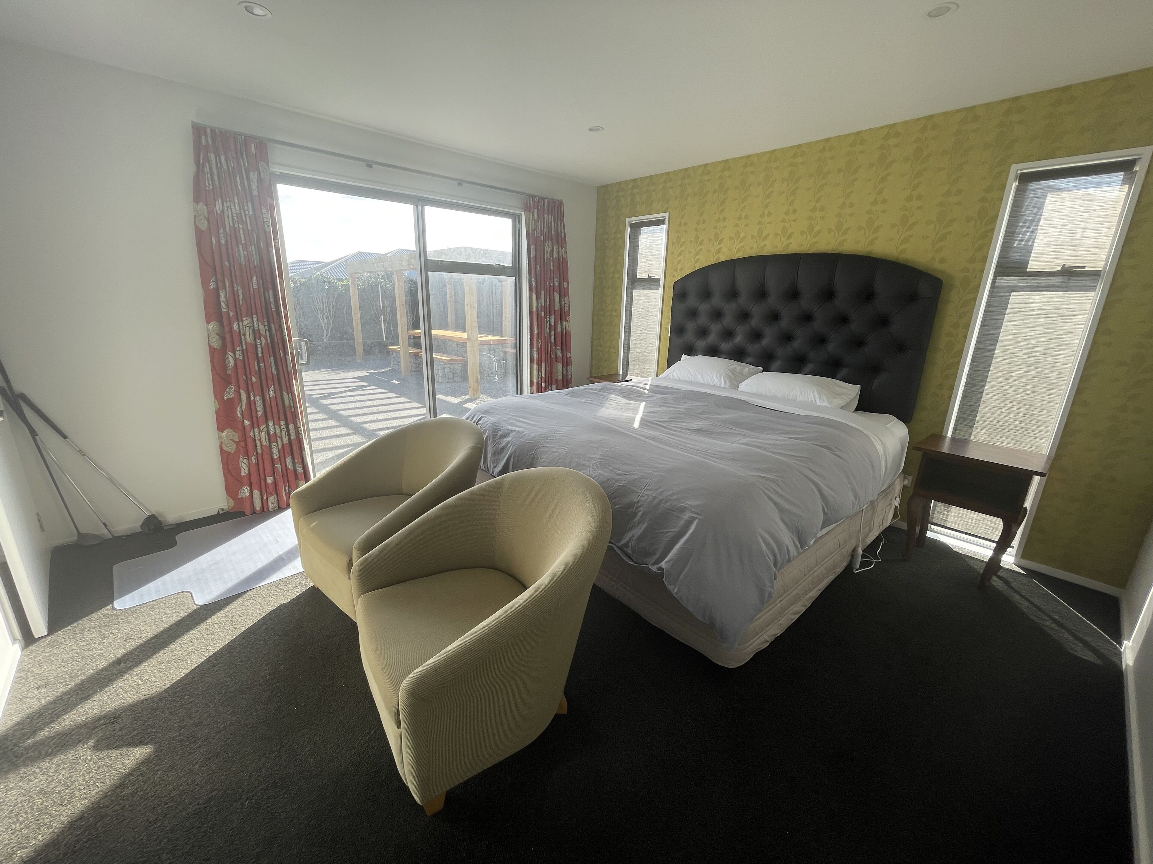 Ein Schlafzimmer mit einem großen Bett, einem Sessel und Blick auf eine Terrasse.