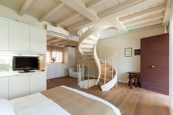 Una habitación de hotel moderna con una escalera en espiral, una cama, un televisor y un escritorio con una silla.
