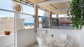 Un balcon avec une table et des chaises, une vue sur la mer et une plante en pot.