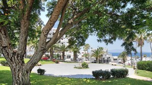 A tree-lined courtyard with a view of the sea and buildings in the background. - Holiday Home 'Estudio 4 Costa Adeje' with Wi-Fi (Adeje)