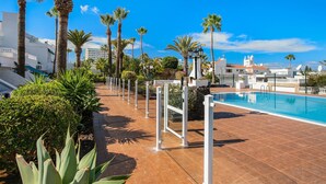 A swimming pool with a tiled deck, surrounded by palm trees and a clear blue sky. - Holiday Home 'Estudio 4 Costa Adeje' with Wi-Fi (Adeje)