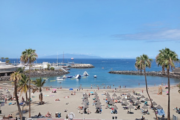 A beach with palm trees, umbrellas, and boats.