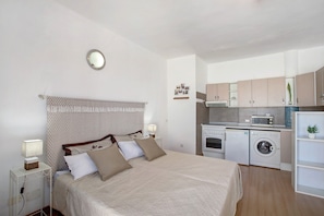 A bedroom with a bed, bedside table, and a small kitchenette with a microwave and washing machine.