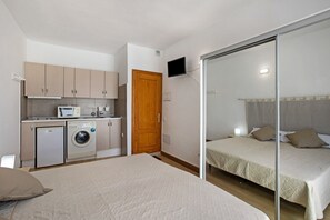 A compact hotel room with a kitchenette, a washing machine, a bed, and a sliding door closet.