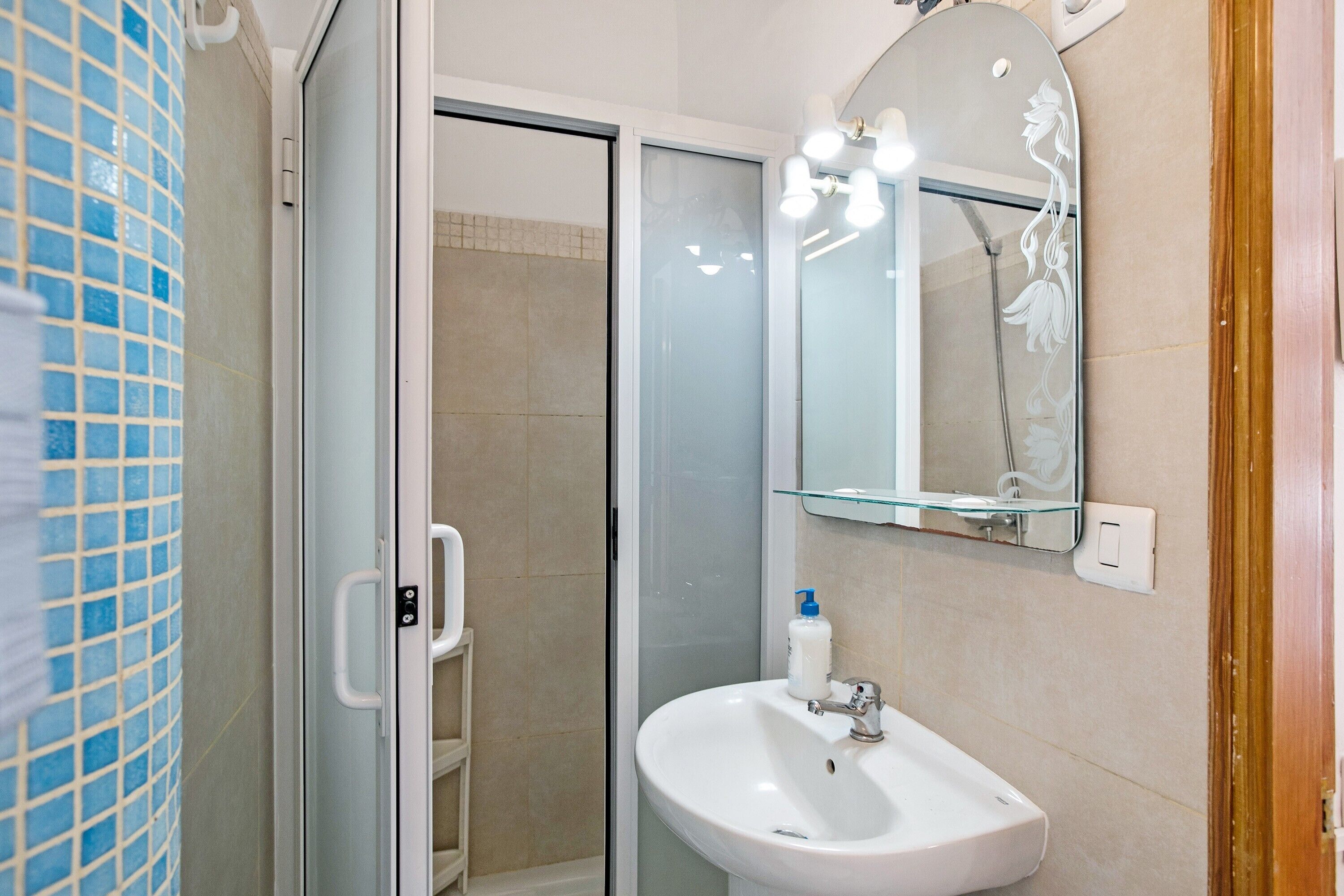 Un bagno con cabina doccia in vetro, lavandino bianco e specchio con illuminazione.