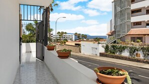 En balkon med plantekasser, klar himmel og udsigt til en gade med bygninger.