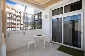 A balcony with a white table and chairs, a sliding glass door, and a view of a building with balconies.