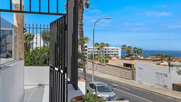 A balcony with a view of a road, a car, and buildings in the distance.